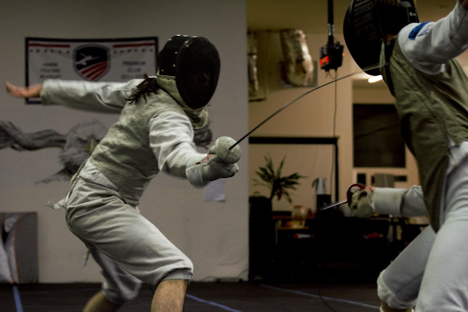 Two masked fencers mid-exchange, one lunging