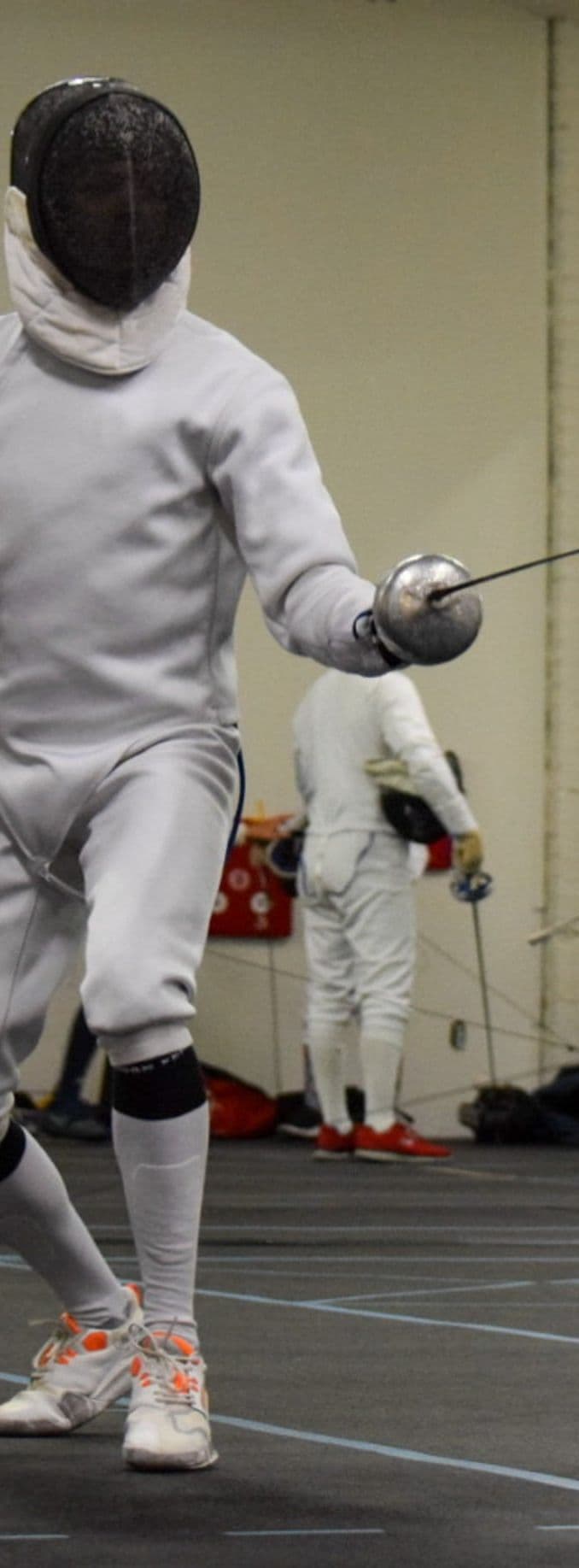 A masked fencer mid-action on the piste