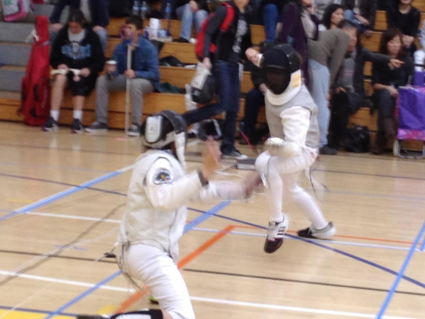 Fencers and families gathered around a strip at a tournament