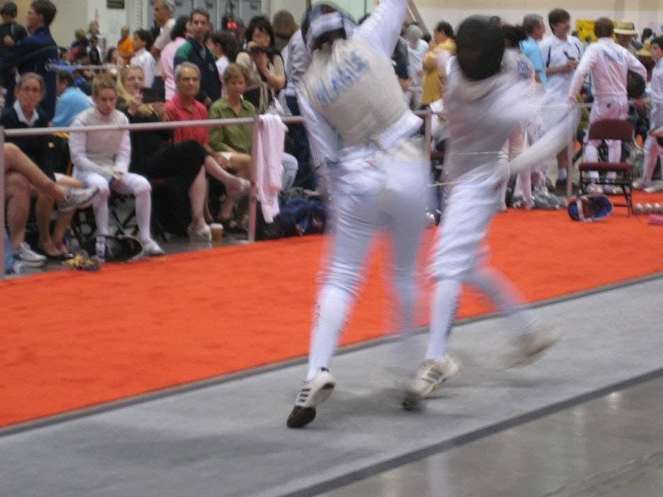 A bout on a competition strip seen from the spectator side, with parents watching from the front row
