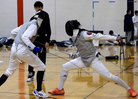Two masked fencers mid-bout at a sanctioned event, one attacking in a full lunge