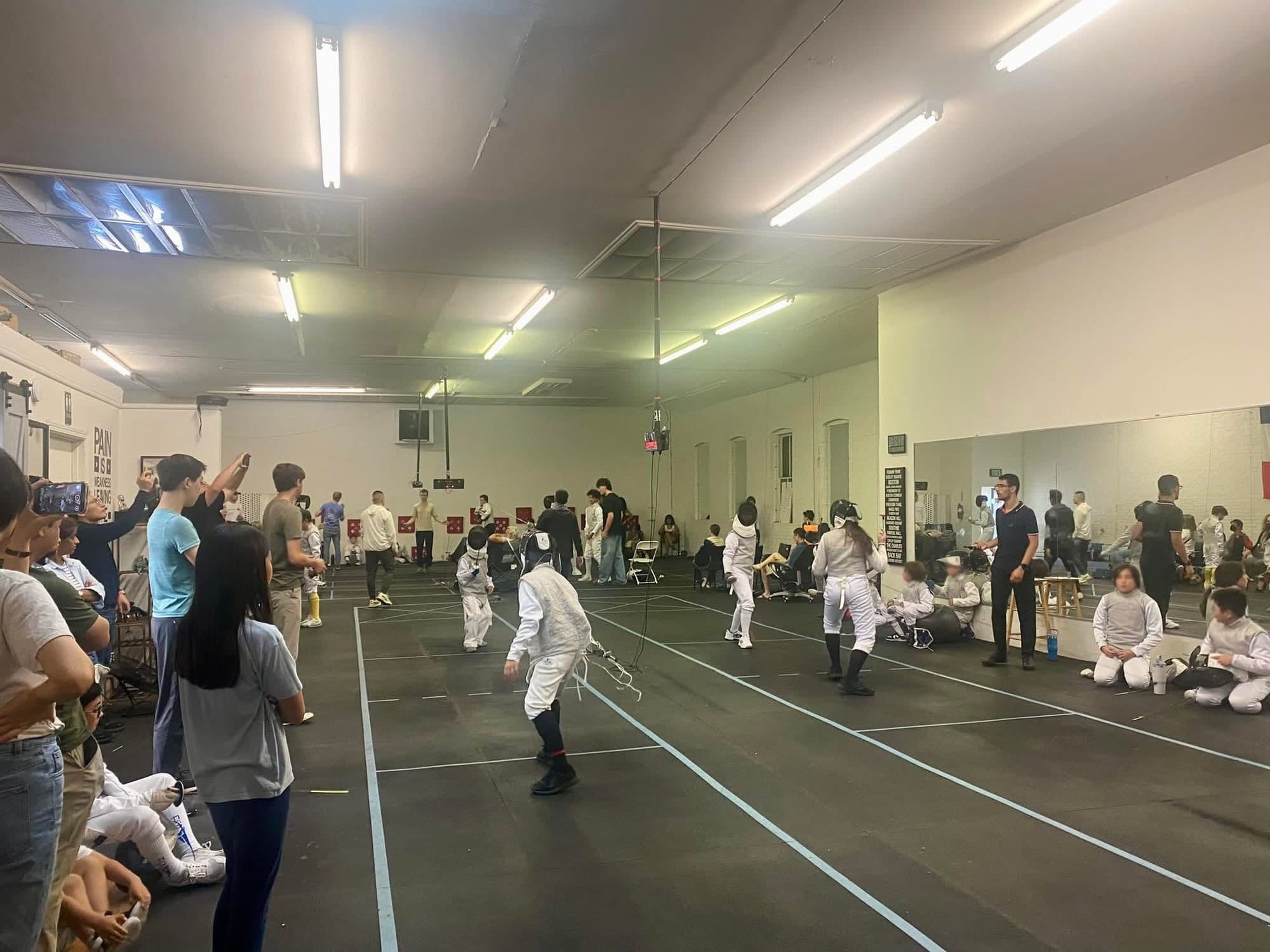 A club tournament under way at Marin Fencing Academy, with bouts running on three strips and families watching from the sides