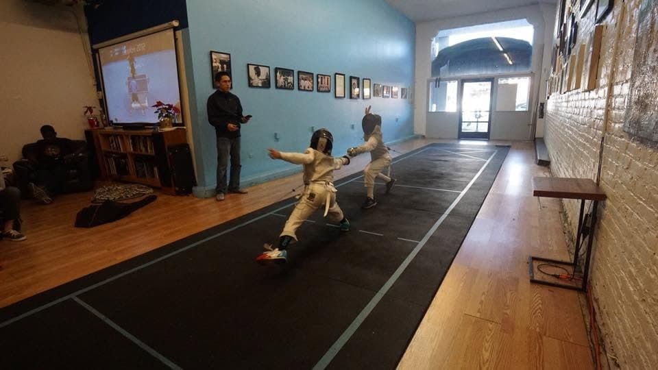Two masked young fencers bouting on the strip at Marin Fencing Academy, a coach watching from the side